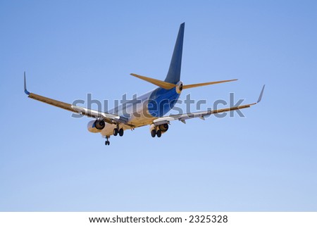 Boeing 737 in completely clear blue sky, with undercarriage and flaps down as it makes its final approach before landing. Seen from side rear.