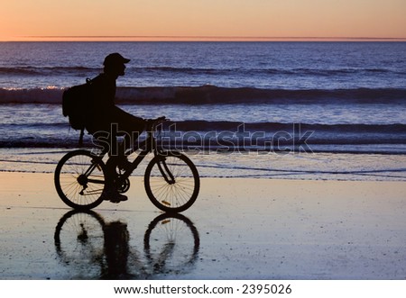 Young man in silhouette riding mountain bike at edge of sea at sunset