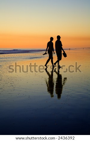 Young couple walking at edge of sea on romantic sunset beach.
