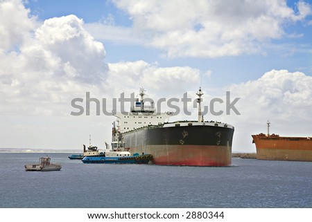 Two tugs pushing a bulk carrier ship to turn it into its berth
