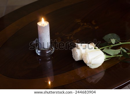 White roses on a wooden dark table with a candle.