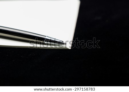 Book note and a pen on black background.