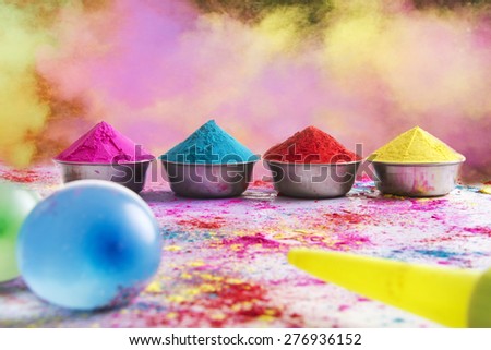Containers of colorful Holi power arranged on floor with squirt gun and water bombs in foreground