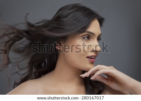 Pretty young female looking away with hair blowing over colored background