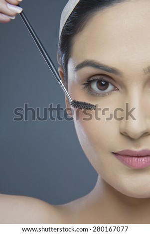 Cropped image of beautiful young woman using eyebrow tinting applicator over colored background