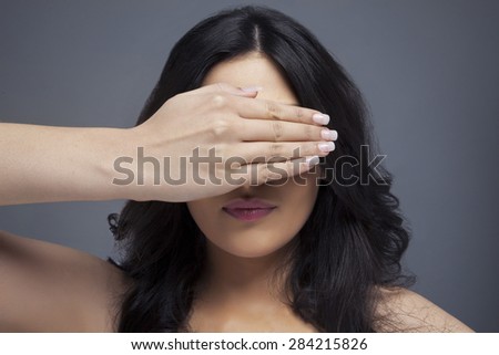 Young female covering eyes her with hand over colored background