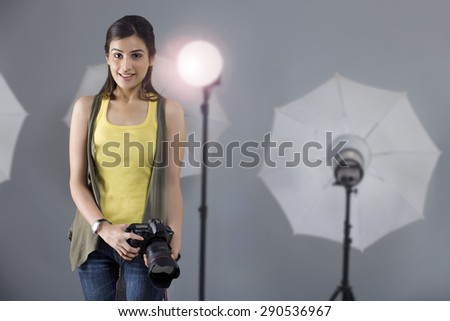 Portrait of young female photographer with camera standing in front of spotlight in studio