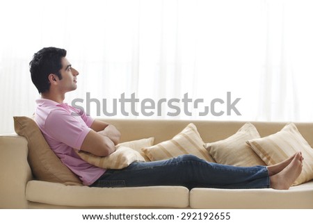 Full length of handsome young man day dreaming on sofa
