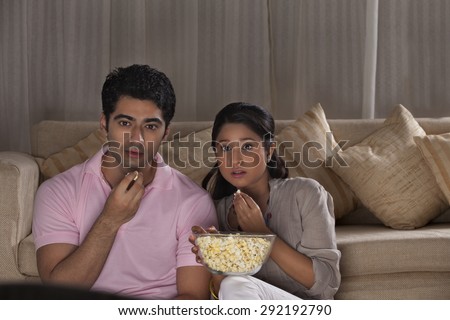 Young scared couple watching movie together at home