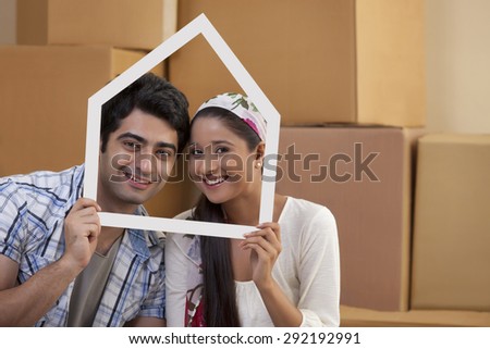 Portrait of smiling young couple looking through a house shaped frame
