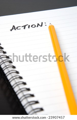 writing ACTION in a spiral-bound notebook. Yellow pencil on blank page
