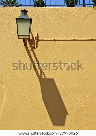 Streetlamp on a wall in Calella de Palafrugell, Catalonia, Spain featuring a strong shadow.