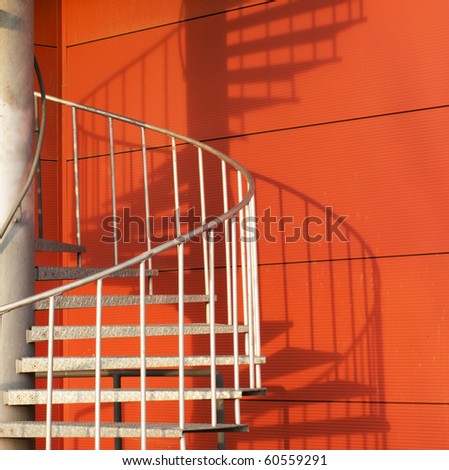 Spiral emergency staircase on side of modern building. Strong sunlight reveals shadow pattern.