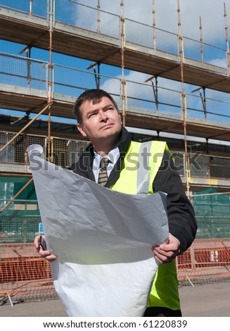 Architect or engineer at work on a building site. Checking plans against the construction work. Confident gaze.