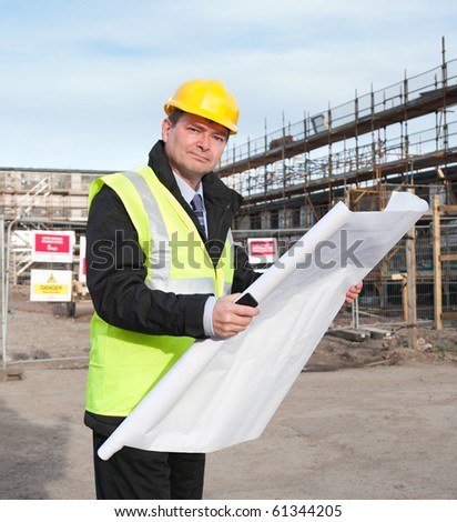 Architect or engineer at work on a building site. Holding plans for construction work. Confident gaze and smile at camera.