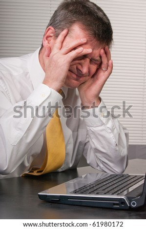 Despairing businessman at laptop and holds head as frustrated and unhappy about news or difficulty. Suffers headache.