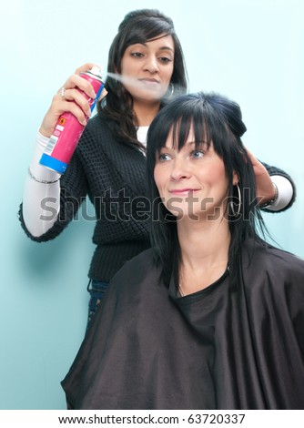 Beautiful young woman receives hairspray from attractive Indian hair stylist