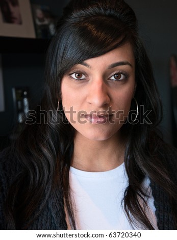 Close up portrait of a lovely young Indian woman looking confidently at the camera with a slight smile. Focus on her eyes and with dark background to highlight her face.