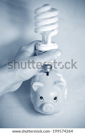 Saving energy concept with hand inserting a light bulb in a piggy bank