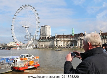 LONDON, UK - MARCH 5, 2011: Senior tourist taking pictures of London\'s Eye on the Thames bank