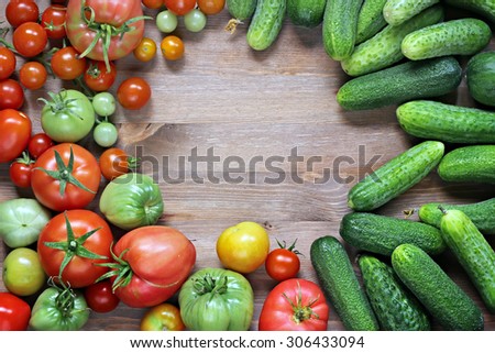 Fresh cucumbers, red and green tomatoes on a table with a blank space in the center in the center, the top view. A place for your text. Tomatoes mature and immature.