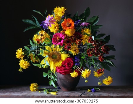 Bouquet from cultivated flowers with a sunflower, roses and other yellow and pink flowers against a dark background and the dragonfly sitting on a table.
