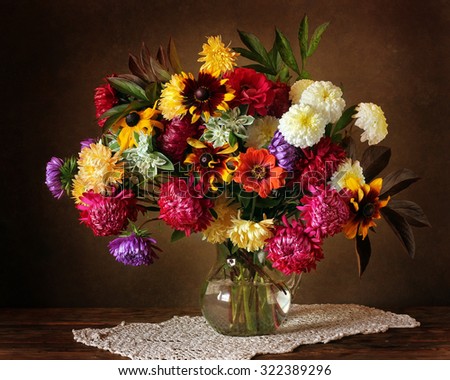 Still life with a beautiful bouquet of cultivated flowers in a glass jug on a dark brown background. Autumn flowers, bouquet as a gift. It is possible to use as a congratulation.