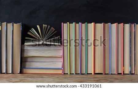 Books in the colored covers on the shelf in the background of a school blackboard. Open book.