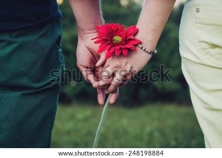 Lovers holding hands holding a flower.