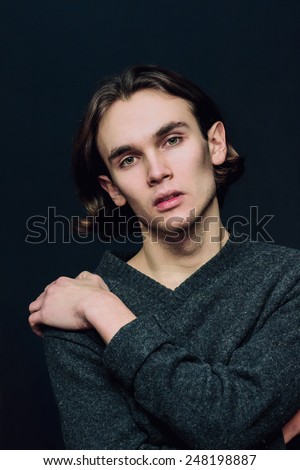 Fashionable long-haired guy standing on a dark background.