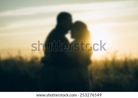 A loving couple standing in a field at dawn adjoined heads backlit . Black and white blur background .