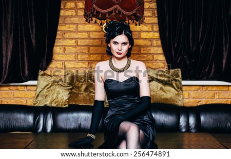 Beautiful girl in black dress sitting on the table. Party in gangster style.