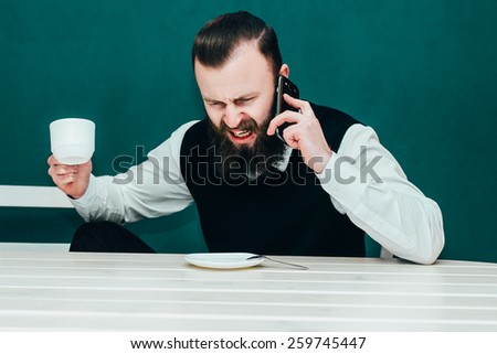Angry businessman shouting into the phone holding a cup of coffee.