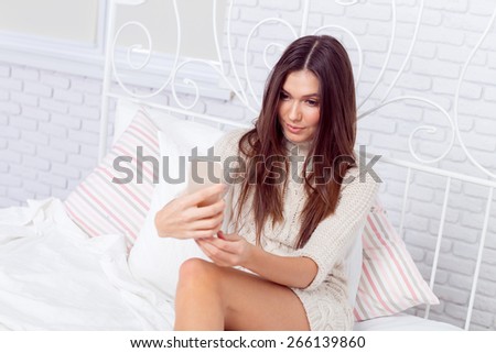 Seductive young woman lying on the bed texting massages on cell phone