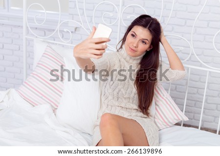 Seductive young woman lying on the bed texting massages on cell phone