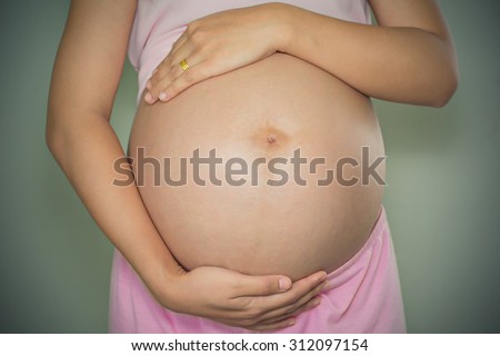 Pregnant Woman holding her hands in a heart shape on her baby bump. Pregnant Belly with fingers Heart symbol. Maternity concept. Baby Shower. Motherhood