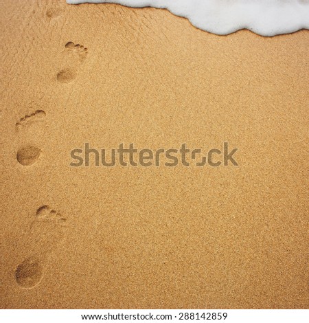 Human footprints in the sand disappearing under a sea wave