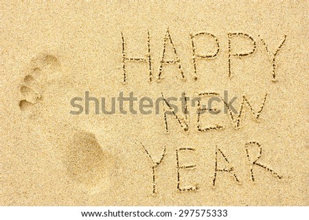 inscription \'HAPPY NEW YEAR\' and human footprint in the sand on the beach