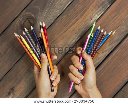 Set of colored pencils in female hands on a background of dark wood tables