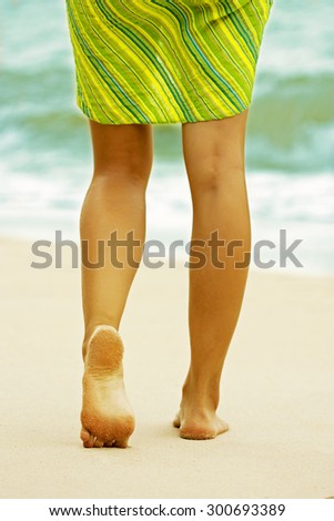 Woman walking on the beach. On the sand footprints remain. Heel close up.