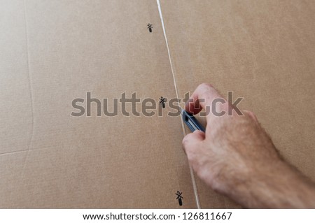 Opening box - man cutting a cardboard box with sharp steel box cutter knife to open it. Concept for parcel delivery, gift opening, moving in, furniture unpacking