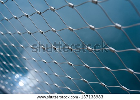 Metallic chain fence link net with blue defocused background. Tilt-shift lense used used to accent the freedom concept and emphasize the attention on them.