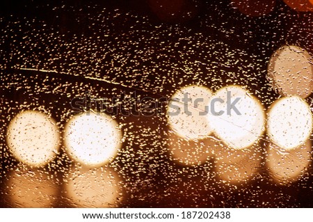 Texture of traffic lights over raindrops on window at night in the city
