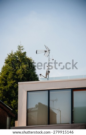 Digital and analog antenna next to satellite dish on the same mast on the rooftoop of a modern building
