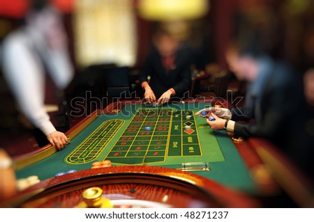 Two men at gaming table collection chip placing bets in a casino assisted by a croupier. Focus is on table. Useful file for your new business, brochure or advertising