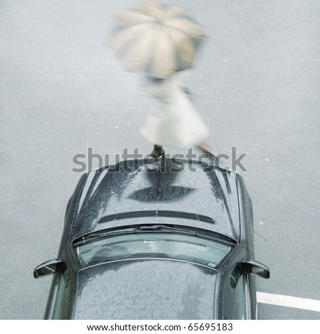 Women with umbrella passing the street in front of a luxury car