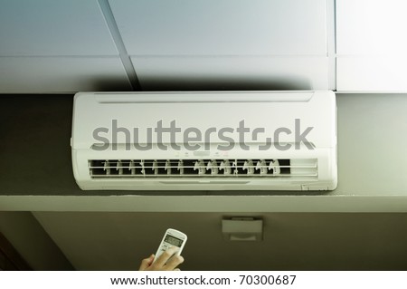 Hand operating remote controller of an air conditioner in modern office.