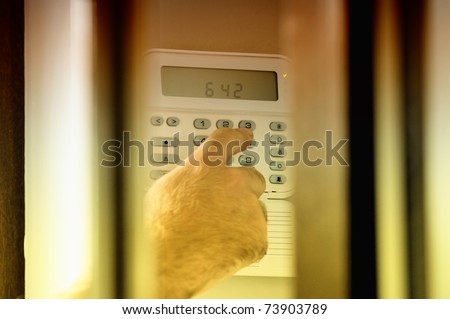 Human hand arming a burglar alarm system. The view is similar as a spy view this situation.