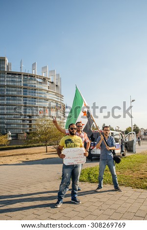 STRASBOURG, FRANCE - AUG 20, 2015: People protesting in front of European Parliament denouncing the Syrian airstrikes on Douma - man holding syrian flag Parliament building in the background