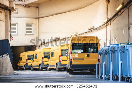 Yellow delivery vans in a row service van, trucks and cars in front of the entrance of a warehouse distribution logistic plant